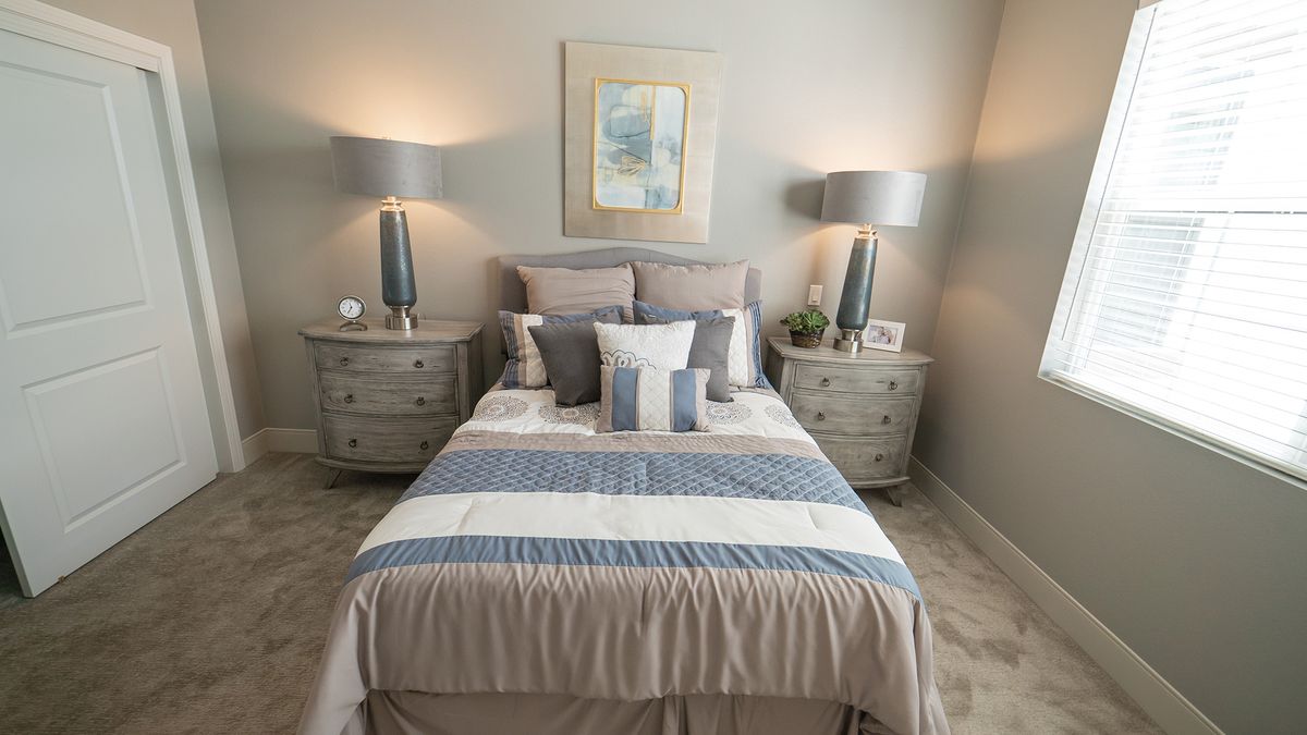 A cozy bedroom with a neatly made bed, flanked by bedside tables and lamps, featuring soft and calming colors.