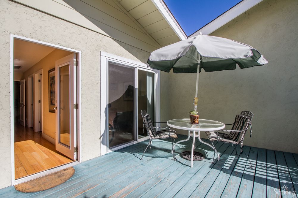 A sunny patio area featuring a round table with chairs and an umbrella, adjacent to a sliding glass door.