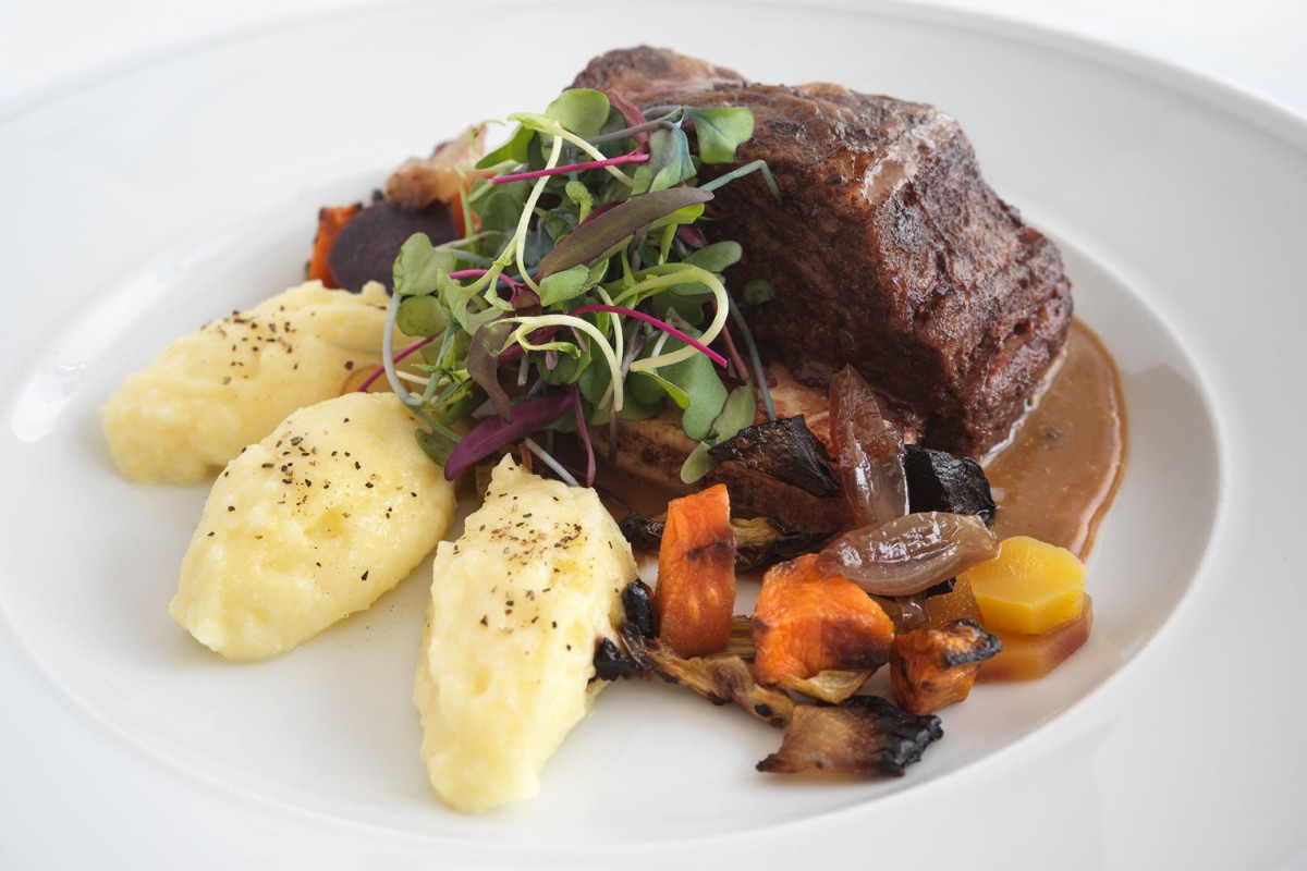 A gourmet beef dish served with mashed potatoes and roasted vegetables, garnished with fresh greens.