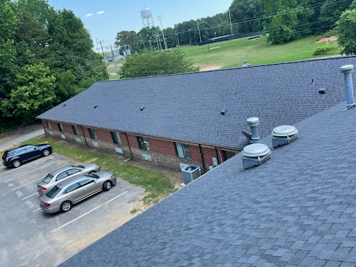 Aerial view of a building's roof with parked cars and a green field in the background.