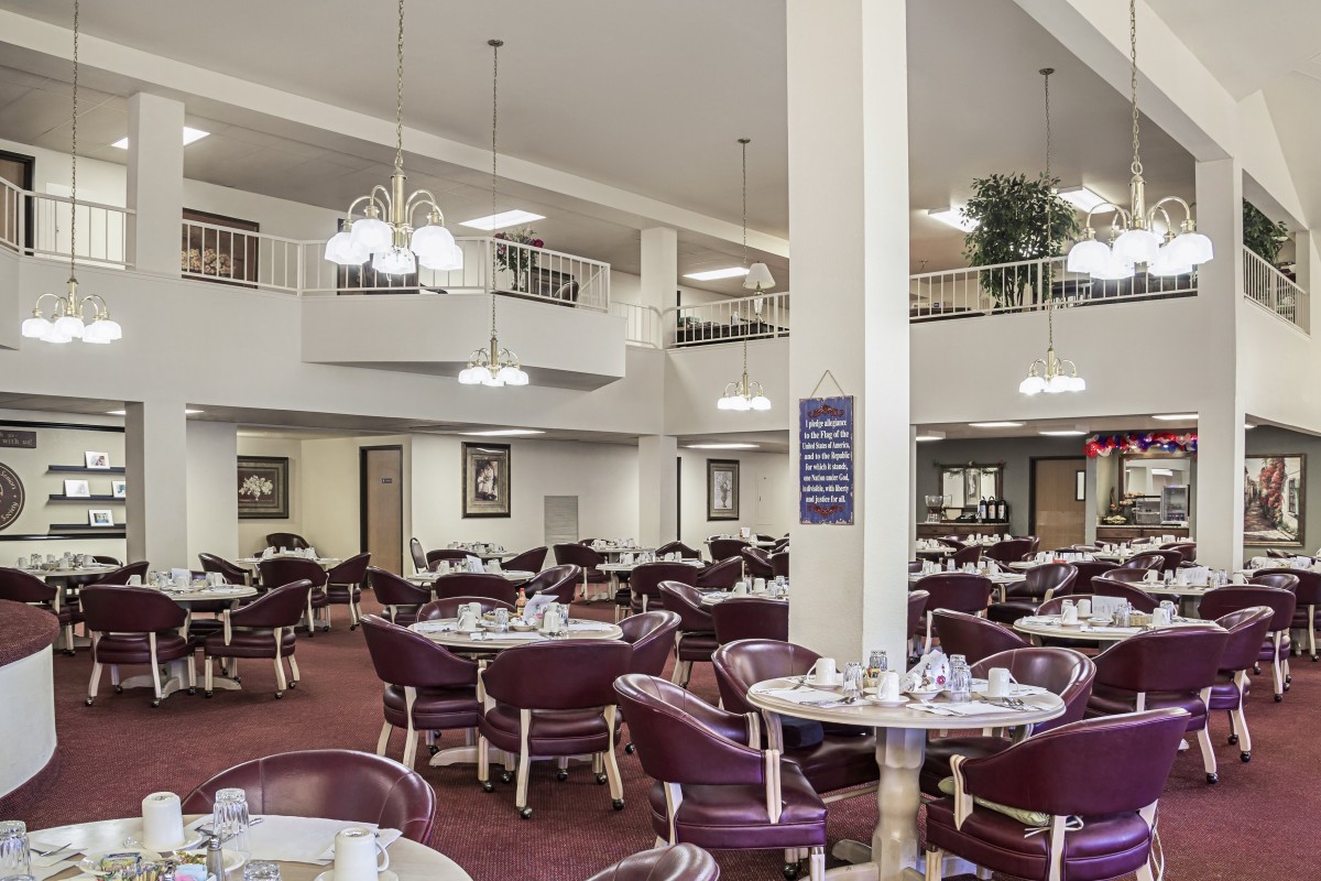 A spacious dining area with multiple tables and chairs, accented by elegant lighting fixtures.