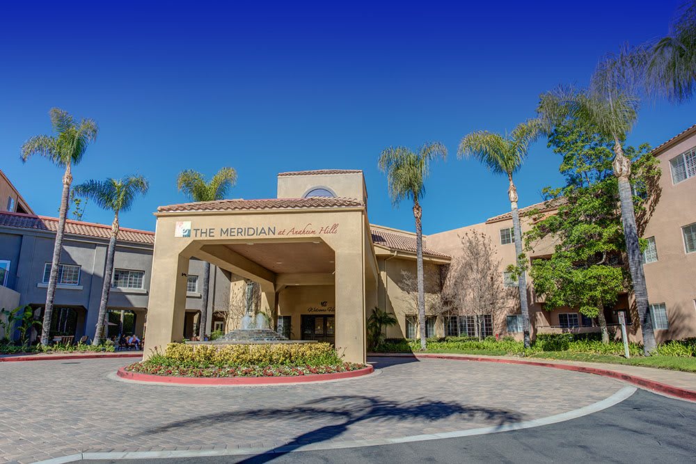 The exterior of a hospital entrance with palm trees and clear blue skies.