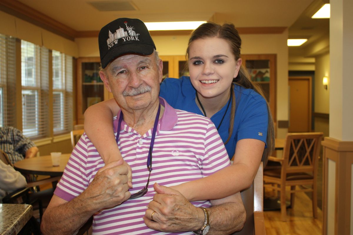 An elderly man and a caregiver share a joyful moment at a nursing home.