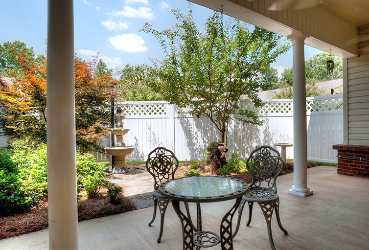 A serene patio with elegant wrought iron furniture surrounded by a lush garden and decorative fountain.