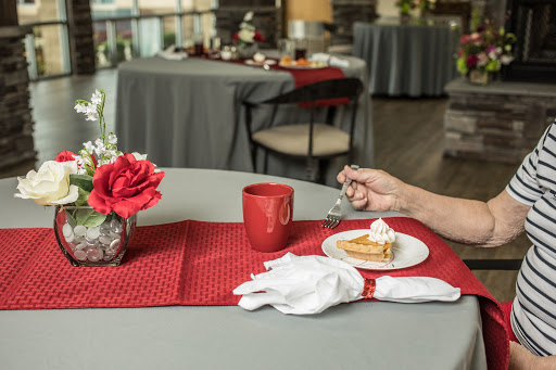 A cozy table setting featuring a slice of cake, a cup of coffee, and a decorative flower arrangement.
