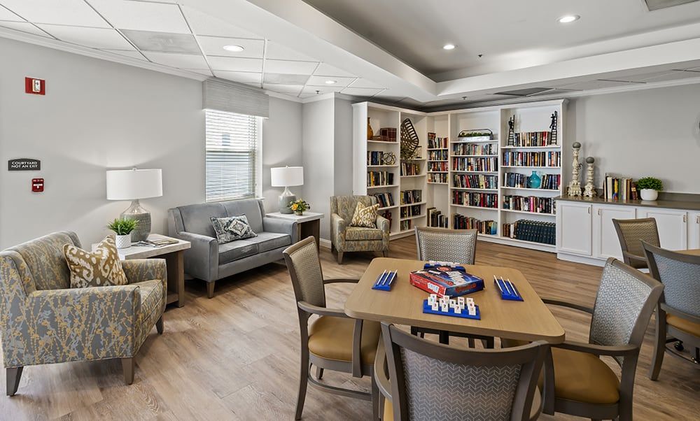 A cozy library room with comfortable seating, bookshelves filled with books, and a table for board games.