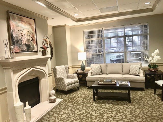 A cozy and elegantly decorated living room with a fireplace, sofa, armchair, and large window.