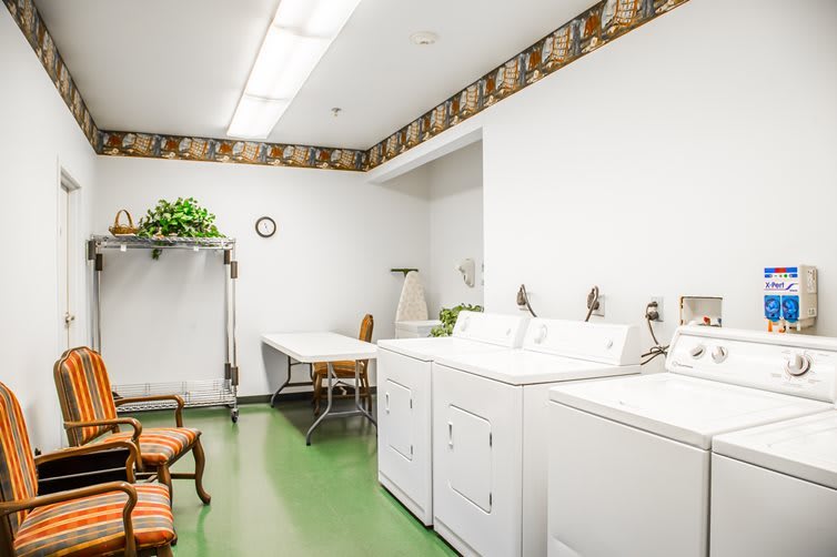 A clean and organized laundry room equipped with washing machines, a dryer, an ironing board, and a chair.