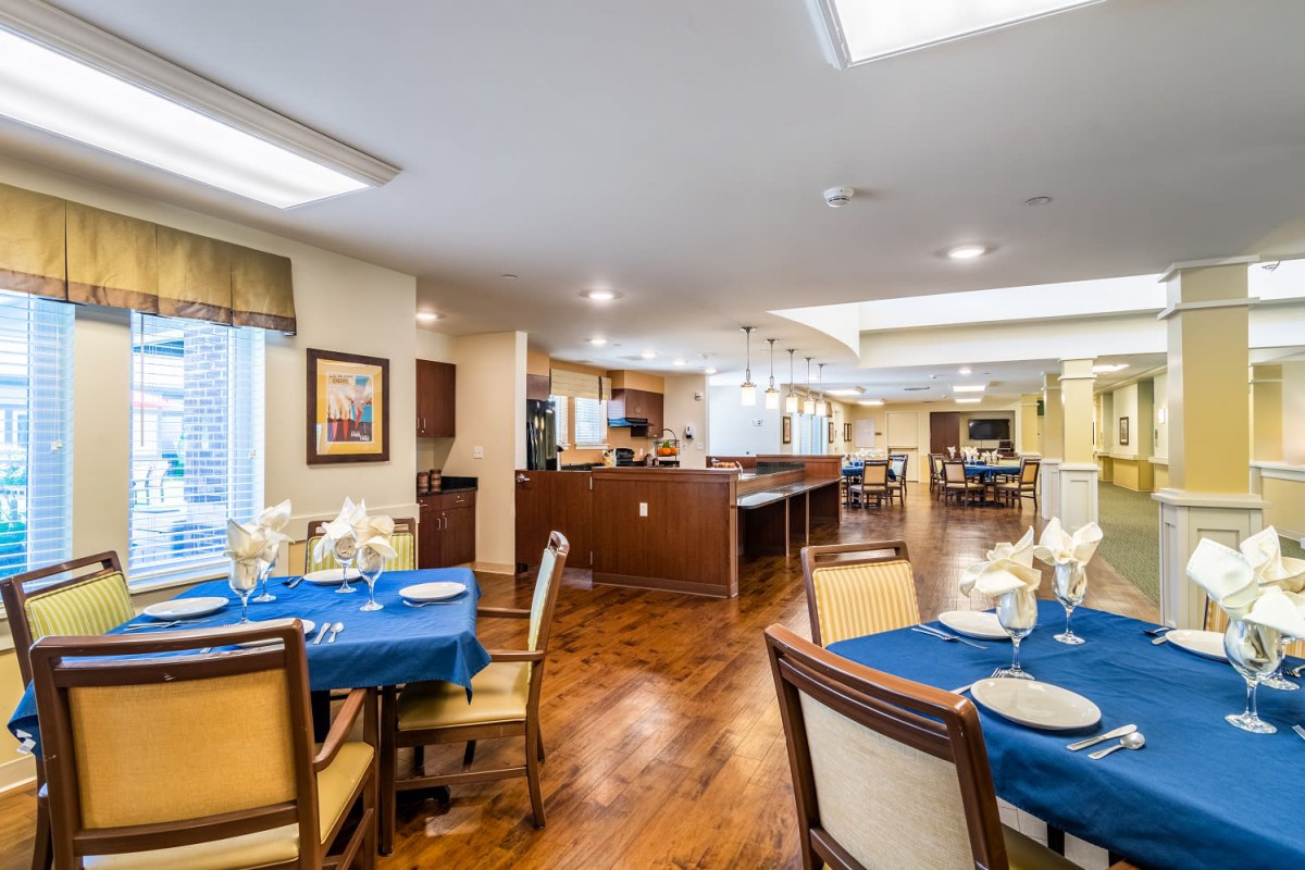 A well-lit dining area with neatly arranged tables and chairs, featuring wooden flooring.