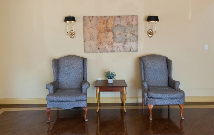 A cozy sitting area featuring two armchairs and a small wooden table with a potted plant, accented by wall sconces and artwork above.