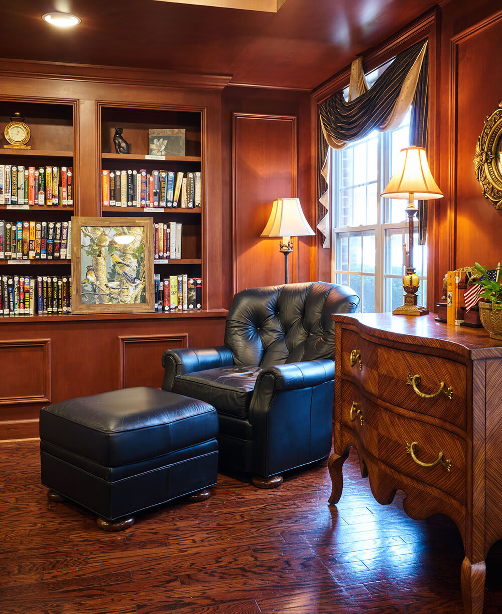 A cozy library corner with a leather armchair and ottoman, surrounded by bookshelves.