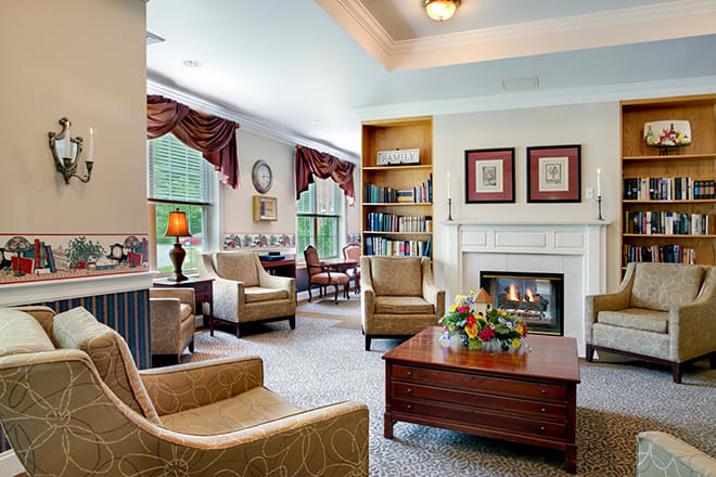 A cozy living room with comfortable armchairs, a central fireplace, and large windows letting in natural light.
