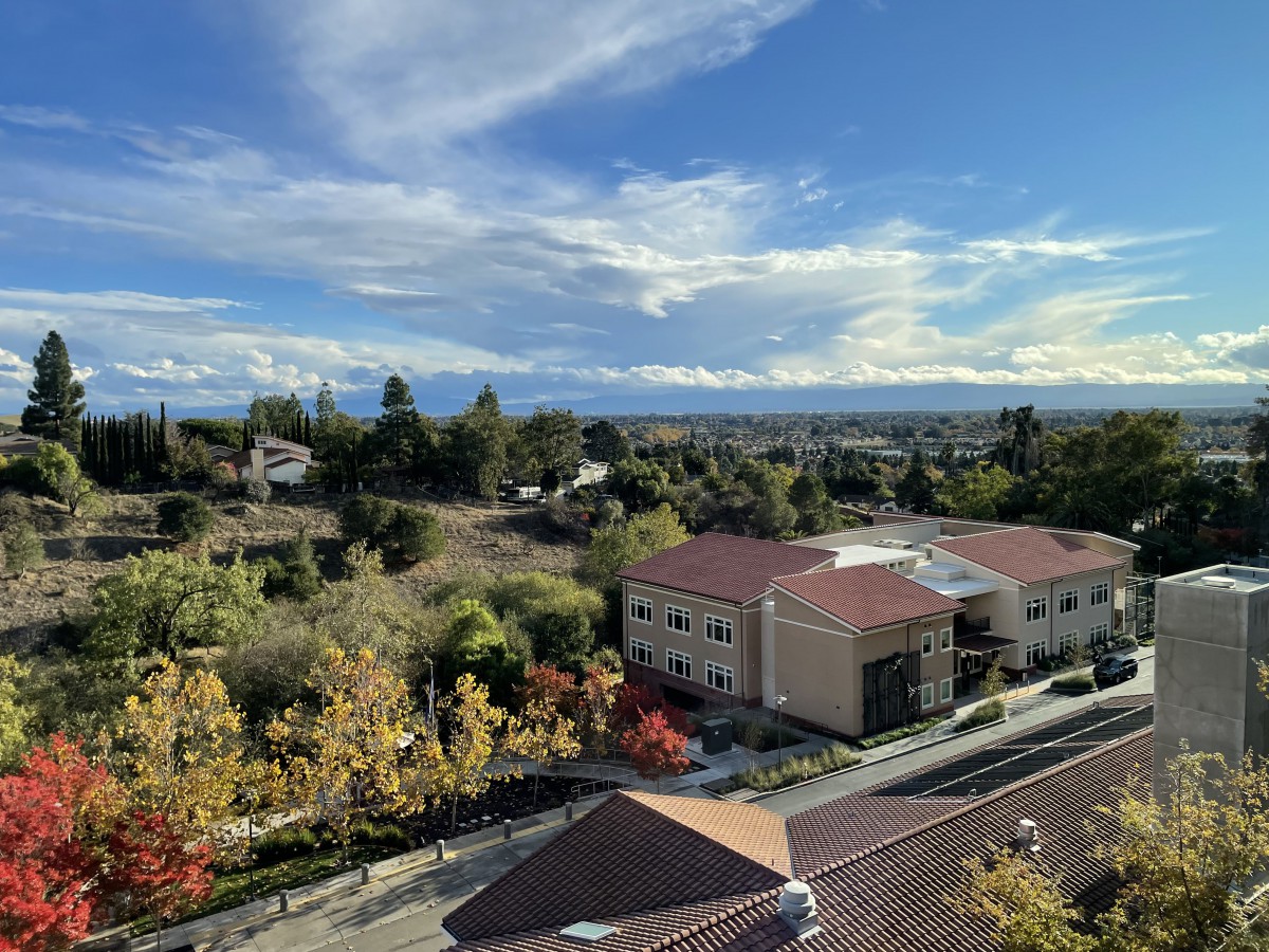 A scenic suburban landscape with buildings, trees, and a clear blue sky.