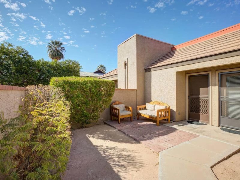 A cozy outdoor patio area with seating arrangements, surrounded by a hedge on a sunny day.