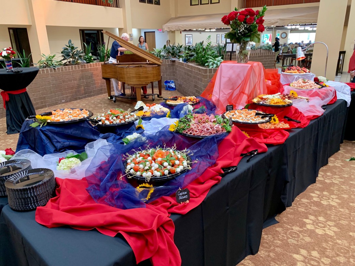 An elegant buffet setup featuring a variety of dishes, with vibrant red and blue drapery, accompanied by a grand piano in an indoor setting.