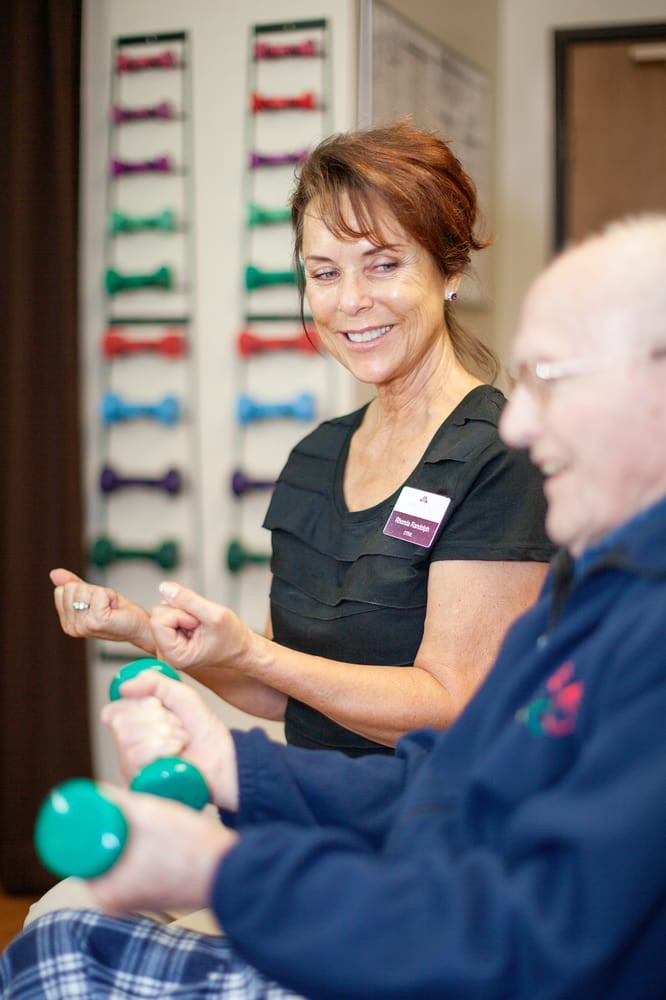 An elderly person exercising with weights under the guidance of a trainer.