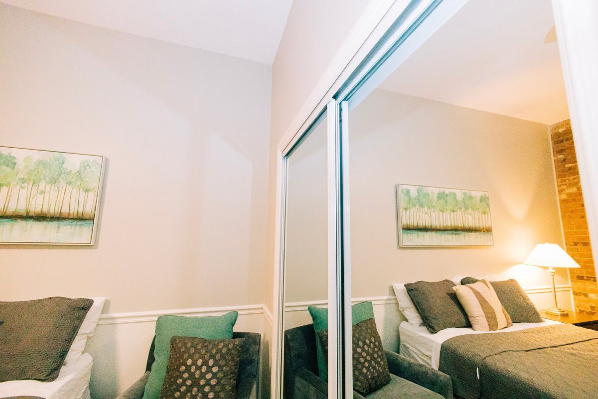 A cozy bedroom with a large mirrored closet and neatly arranged pillows.