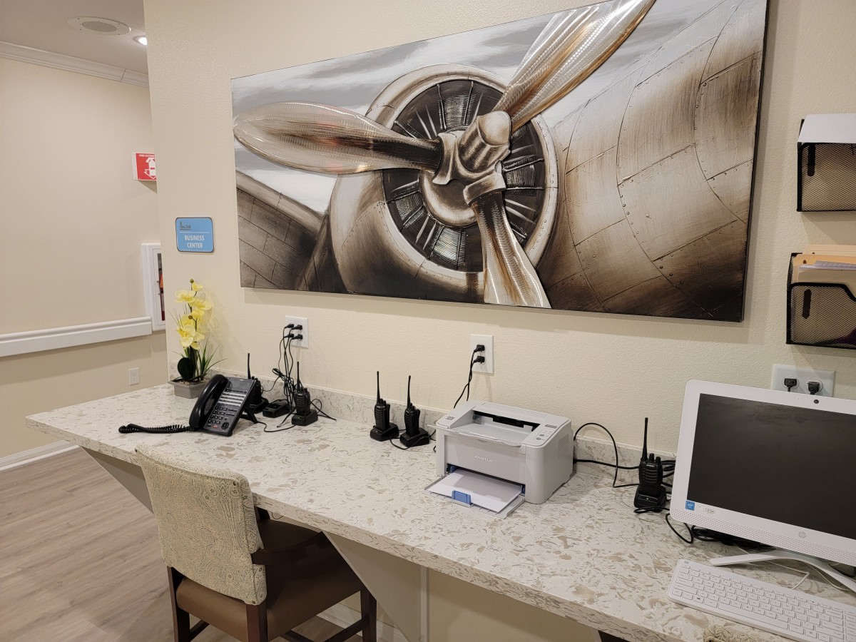 An office workstation equipped with communication devices, a printer, and computer, featuring an aeronautical-themed painting.