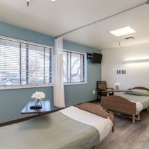 A clean and well-lit hospital room with two beds and a window view.