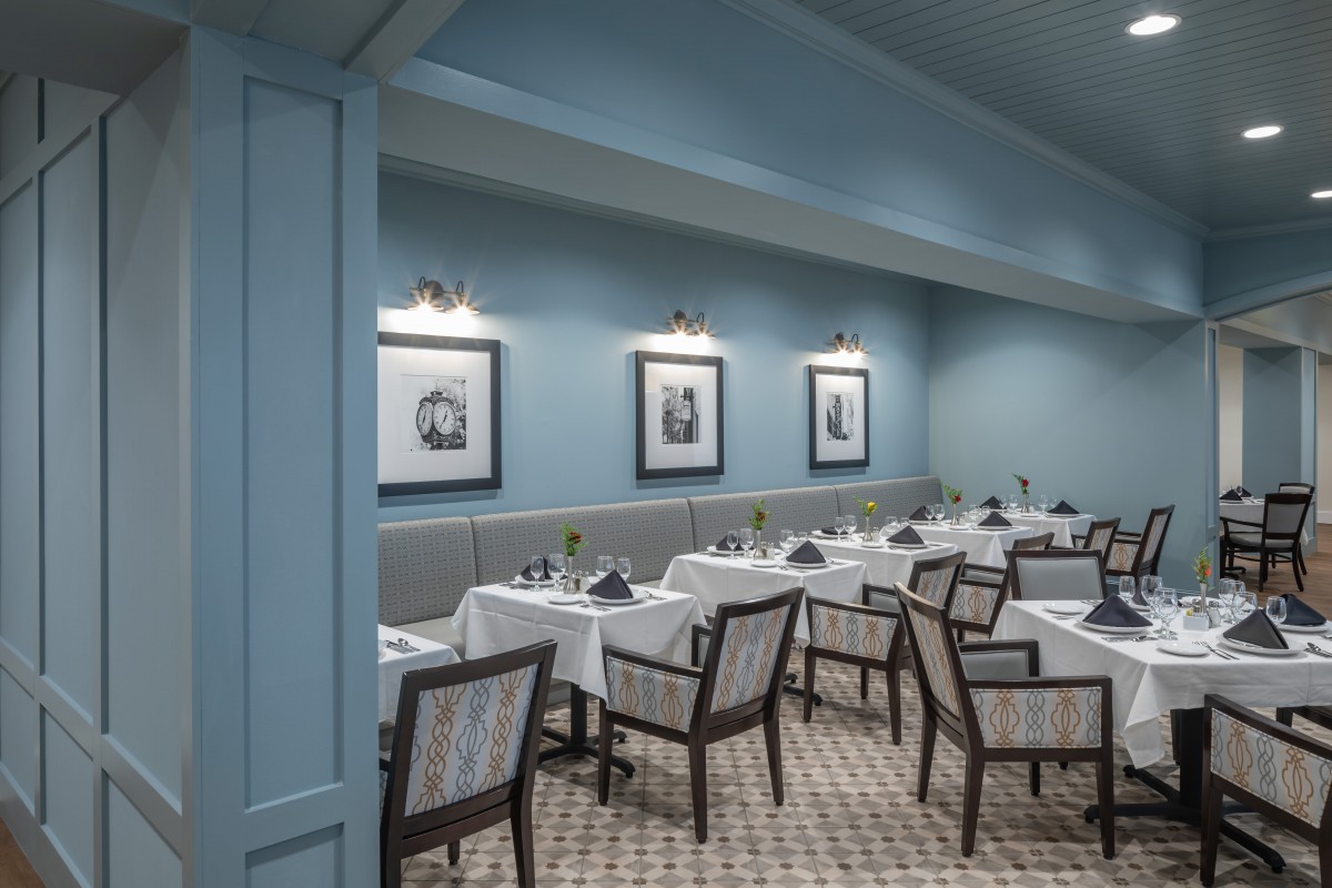 A tastefully designed restaurant dining area with blue walls, neatly arranged tables and chairs, and framed artwork.