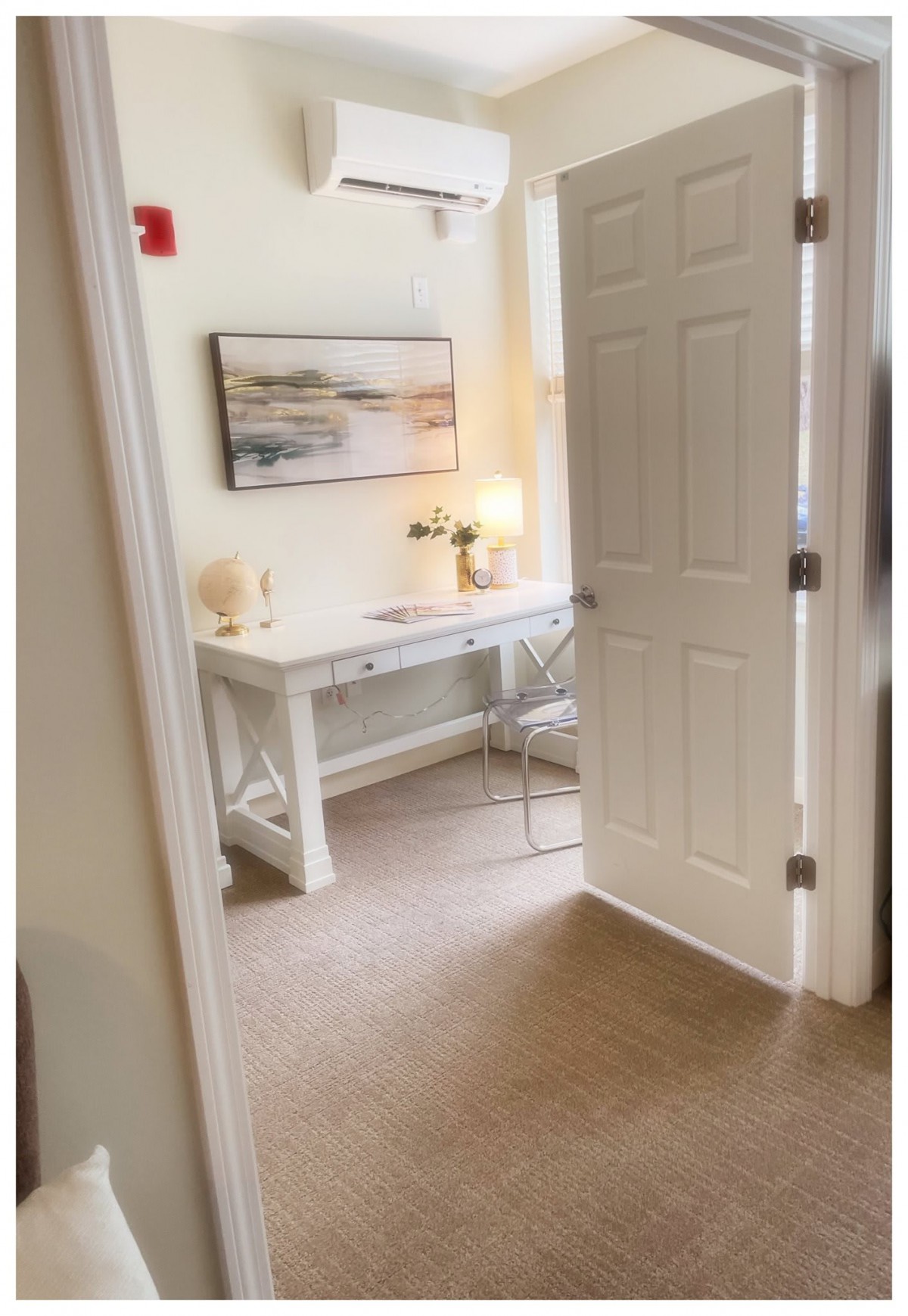 A cozy home office setup with a desk, chair, and lamp next to an open door.