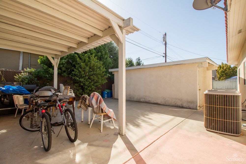 A sunny backyard patio area with bicycles, chairs, and a pergola.