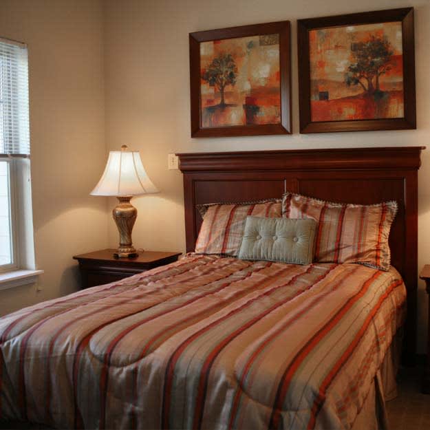 A cozy bedroom with a striped bedspread, decorative pillows, side tables with lamps, and artwork hanging above the bed.