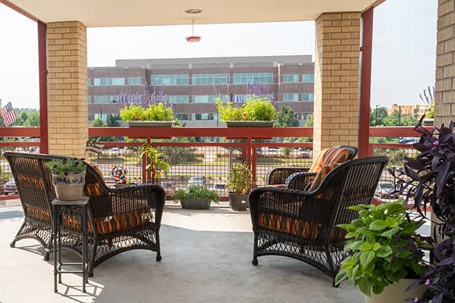 A cozy balcony with wicker chairs and potted plants overlooking a modern building.