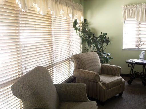 A cozy corner of a living room featuring two comfortable chairs, light filtering through window blinds, and a small indoor plant.
