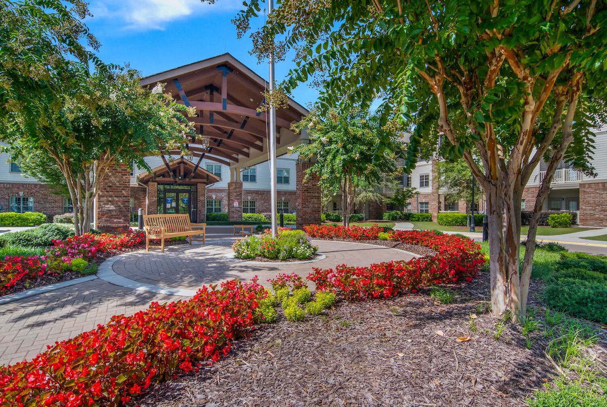 A beautifully landscaped entrance to a brick building, surrounded by colorful flowers and lush trees.