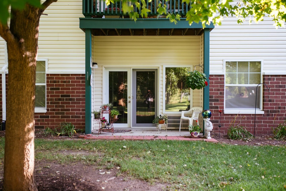 A cozy patio area with a glass door, surrounded by brick walls and adorned with outdoor furniture and plants.
