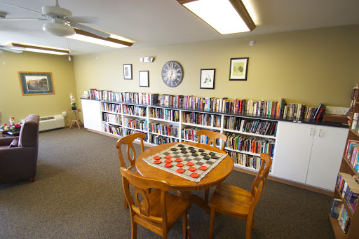 A cozy library space featuring bookshelves filled with books, a wooden table with a board game, and comfortable seating.
