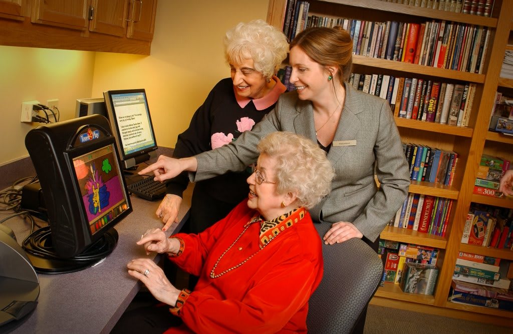 Three women engaging with a computer in a library setting.