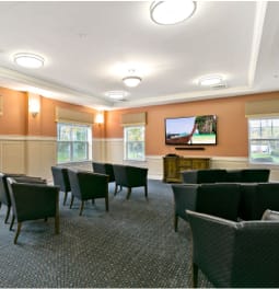 A meeting room with chairs facing a television and windows letting in natural light.