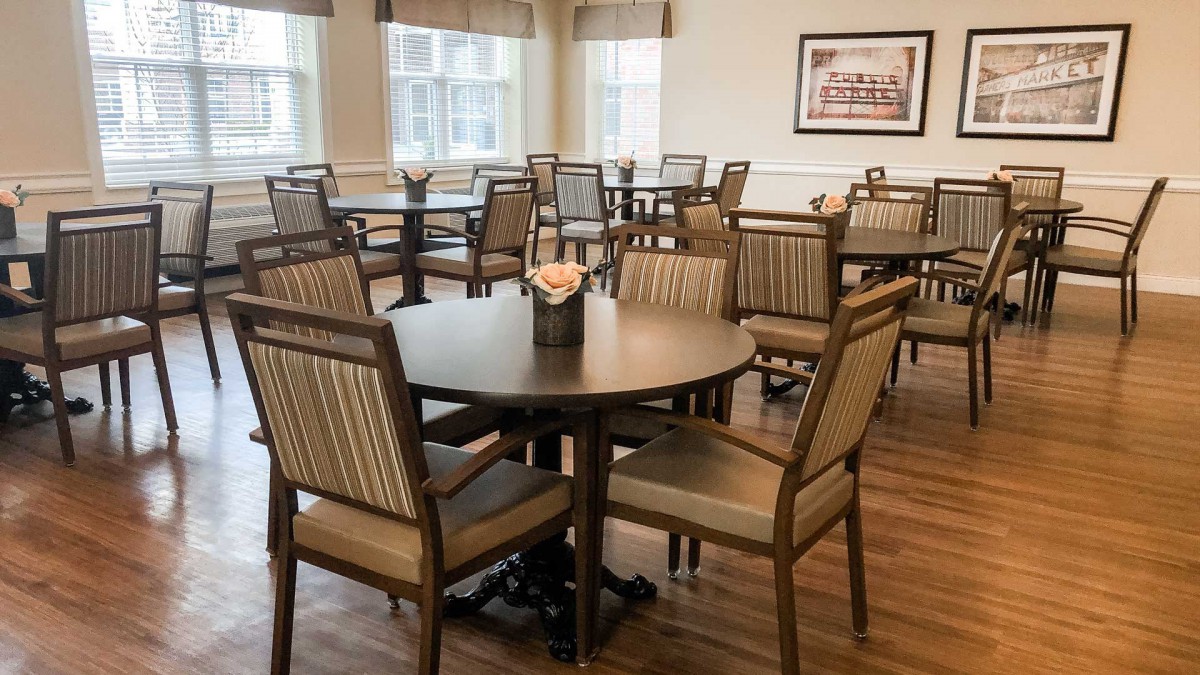 A dining area with neatly arranged tables and chairs, featuring wood flooring and a framed picture on the wall.