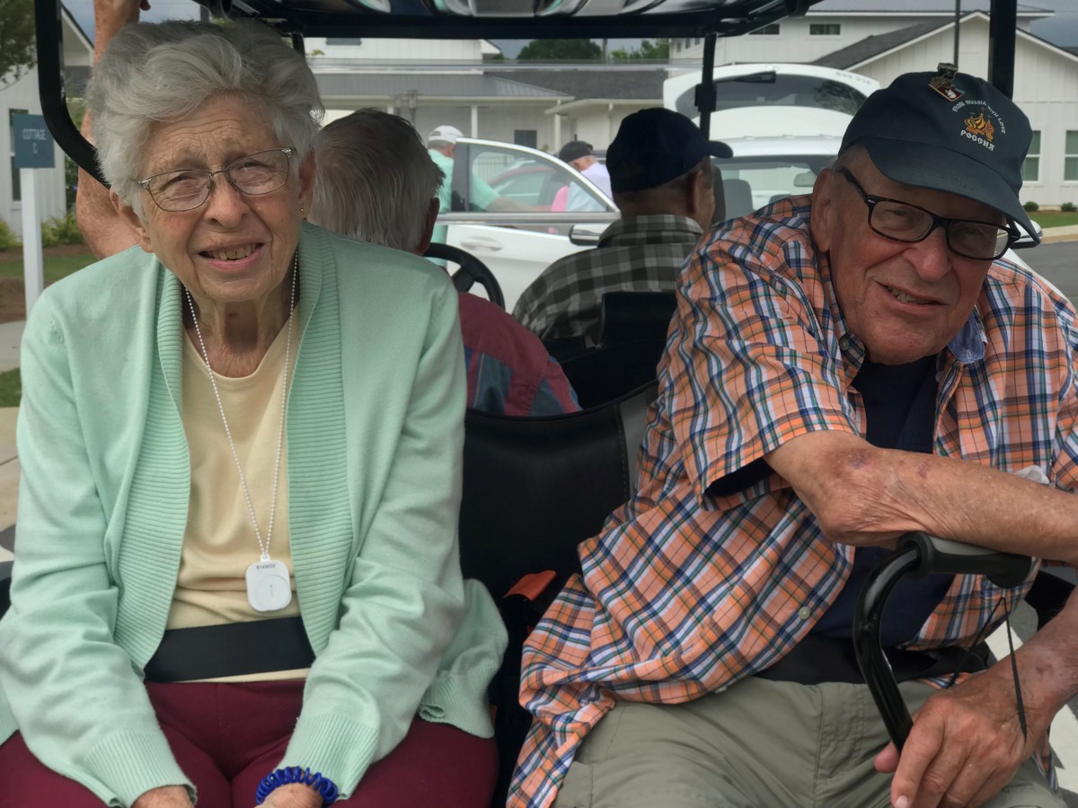 An elderly couple smiling while seated in a golf cart outdoors.