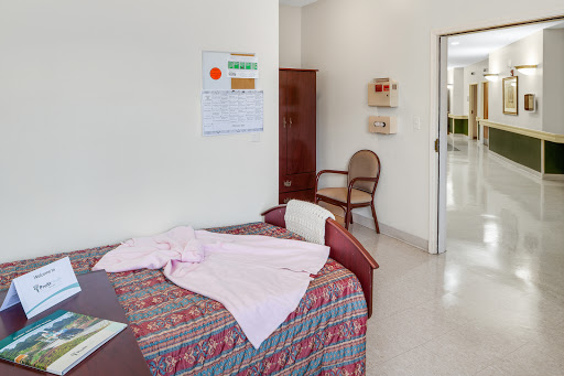 A tidy bedroom featuring a bed with colorful bedding, a chair, and a wall calendar.