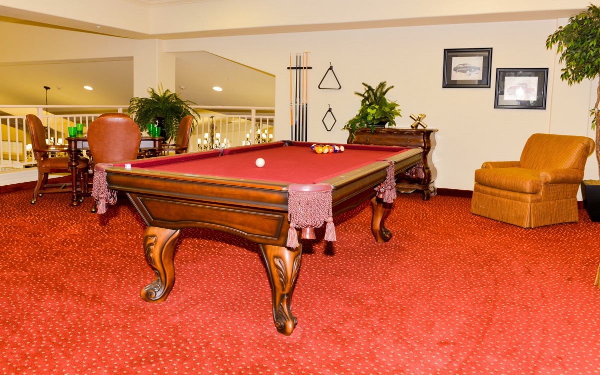 A stylish game room featuring a wooden pool table with a red felt top, set on a vibrant red carpet, surrounded by plants and decor.