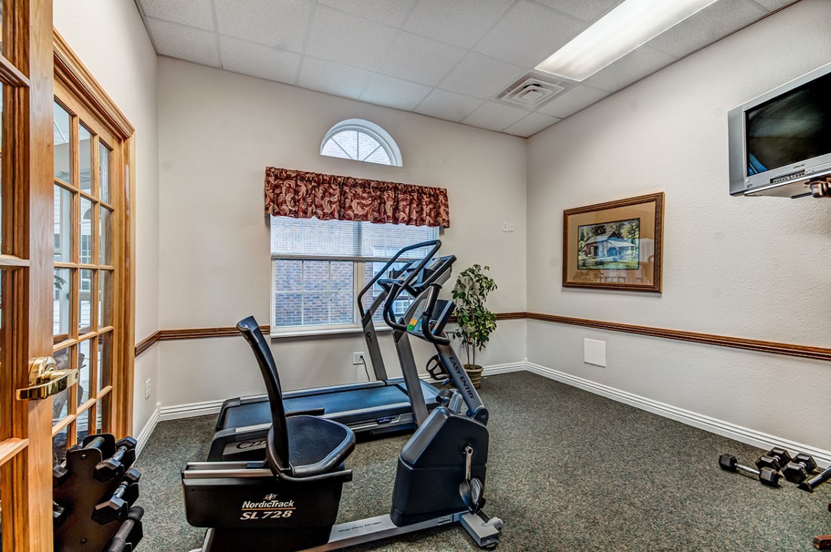 A small fitness room with a treadmill and exercise bike next to a window.