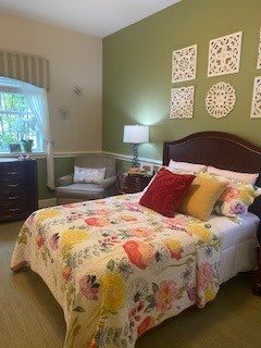 A cozy bedroom featuring floral bedding and decorative pillows, with wall art and a table lamp adding charm to the space.