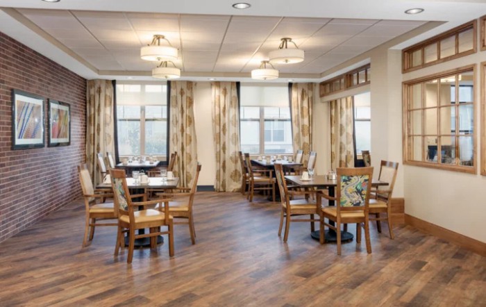 A well-lit dining area with wooden flooring and elegantly arranged tables and chairs.