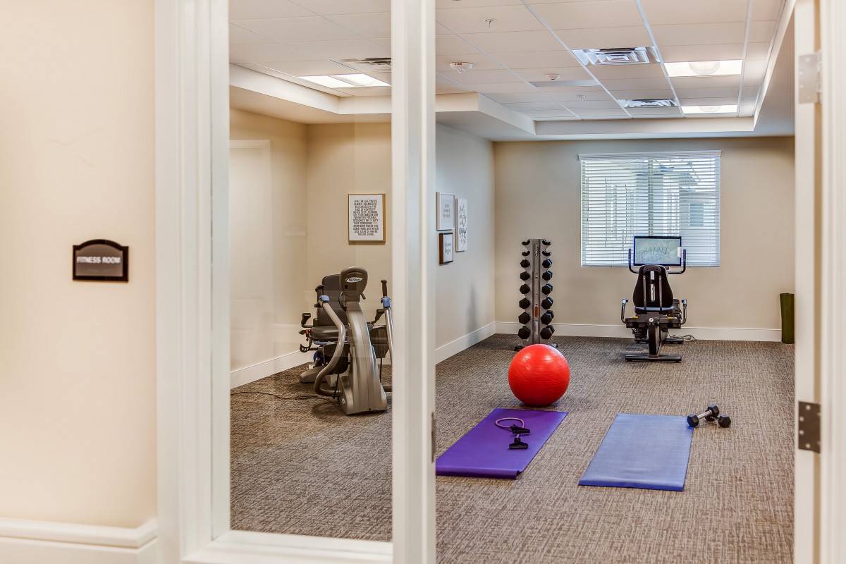 A small fitness room with exercise equipment including yoga mats, dumbbells, an exercise bike, and a stability ball.