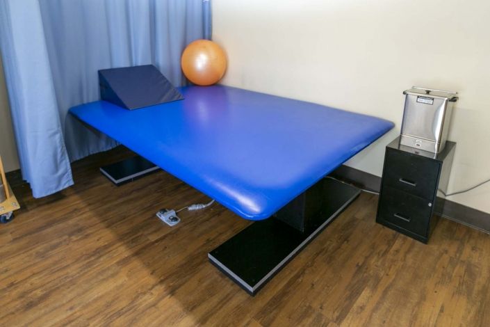 A physical therapy room featuring a blue therapeutic table and an exercise ball.