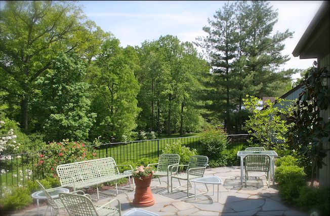 A serene patio with outdoor furniture overlooking a lush garden and trees.