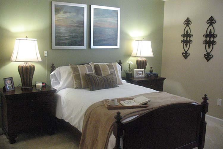 A cozy bedroom with a neatly made bed, soft lighting from table lamps, and artwork on the walls.