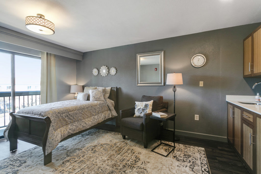 A modern bedroom with grey walls, featuring a cozy bed, an armchair, and stylish lighting.