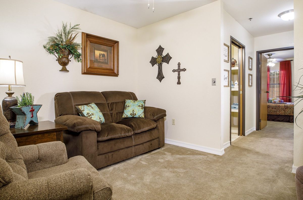 Cozy living room with a brown sofa, armchair, and wall decorations including crosses and a plant.