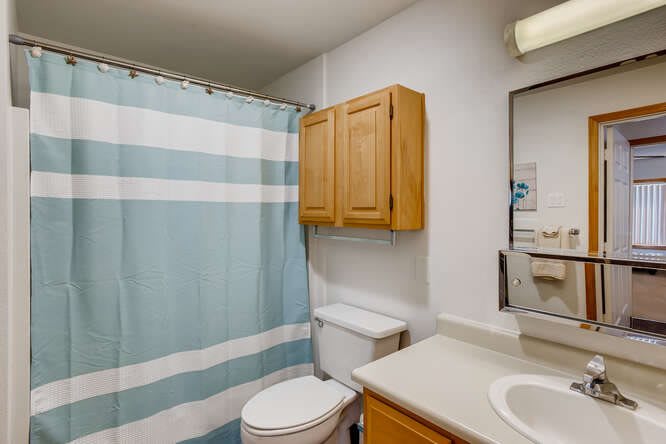 A clean and organized bathroom with a striped shower curtain and wooden cabinets.
