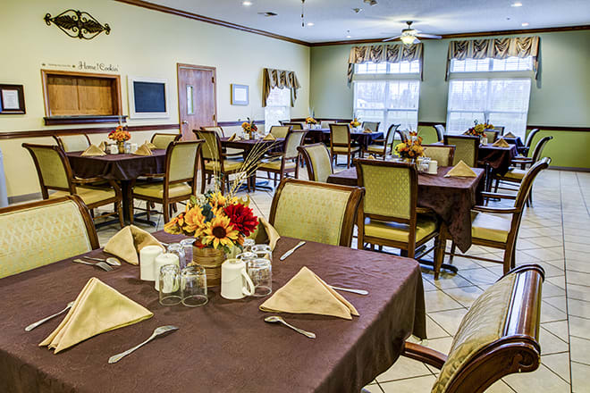 A well-organized dining room with neatly arranged tables and chairs, featuring floral centerpieces and napkins.