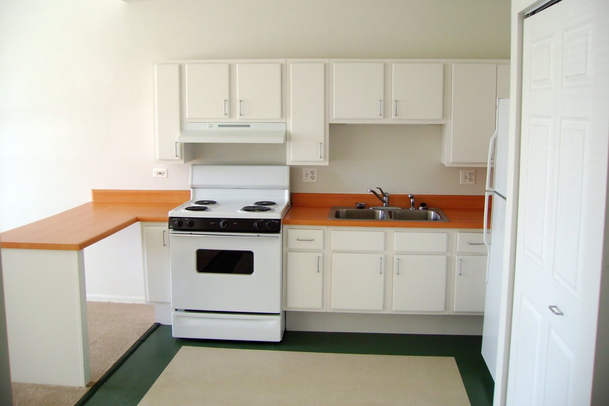 A simple kitchen with white cabinets, a stove, an oven, a sink, and a refrigerator.
